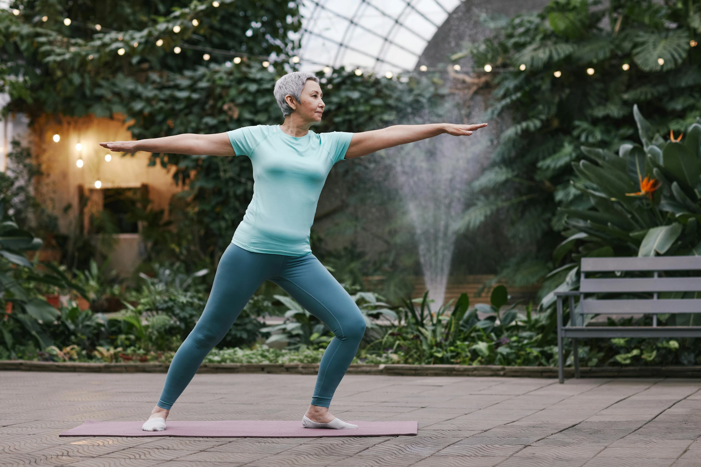 a woman standing on a yoga mat doing a yoga pose, a statue, pexels contest winner, botanic garden, older woman, thumbnail, low quality photo