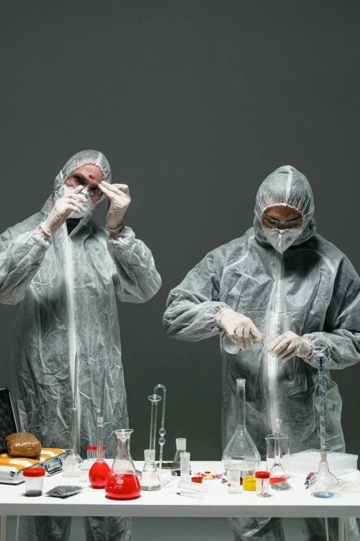 a couple of people that are standing in front of a table, pexels contest winner, plasticien, hazmat suits, taking mind altering drugs, on grey background, russian lab experiment