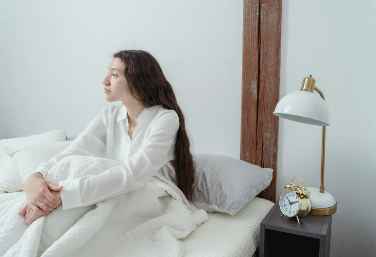 a woman sitting on top of a bed covered in a blanket, trending on pexels, happening, clothed in white shirt, insomnia, extremely long hair, wearing lab coat and a blouse