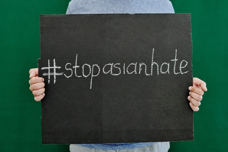 a person holding a sign in front of a green wall, trending on unsplash, asian origin, hate, background image, chalkboard