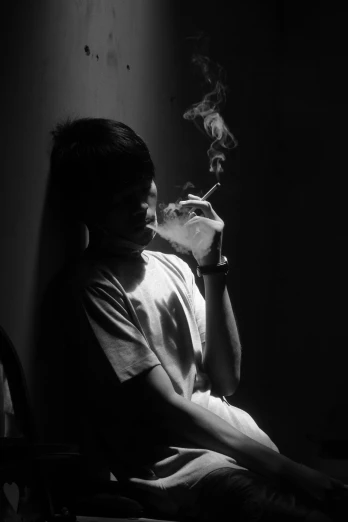 a man smoking a cigarette in a dark room, a black and white photo, unsplash, teenage boy, thawan duchanee, young boy, back - lit