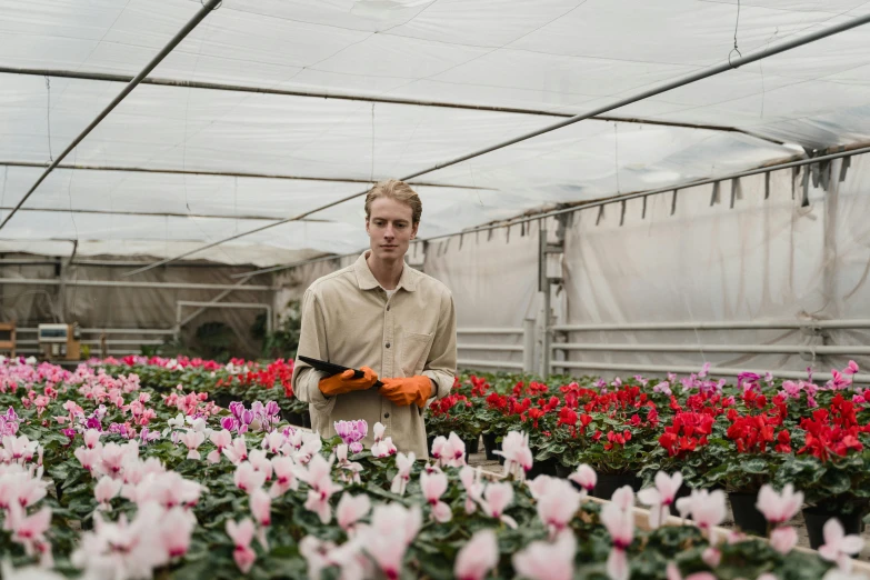 a man standing in a greenhouse holding an orange glove, pexels contest winner, flower sepals forming helmet, lachlan bailey, in rows, architectural and tom leaves
