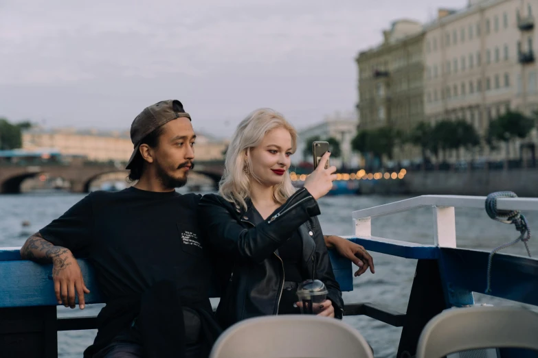 a man and a woman sitting next to each other on a boat, by Julia Pishtar, surrounding the city, viktoria gavrilenko, pointing at the camera, a blond