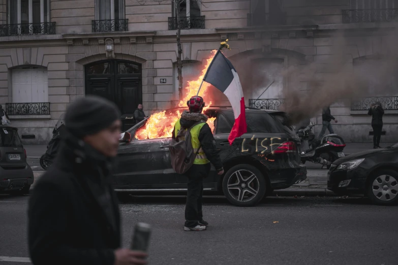 a man standing in front of a burning car, a cartoon, by Benjamin Block, pexels contest winner, les automatistes, french flag, people on the streets, coloured photo, a person standing in front of a