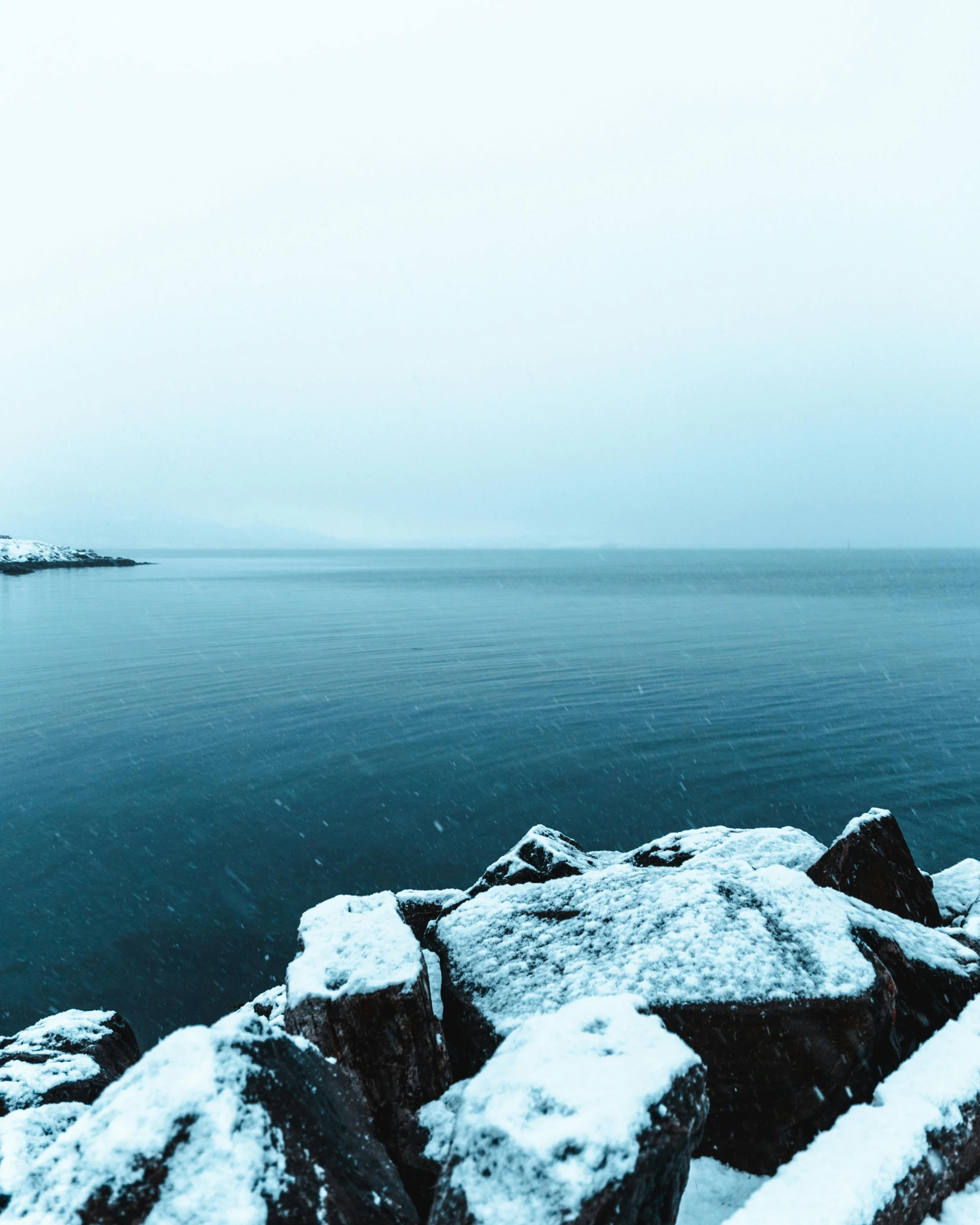 a large body of water surrounded by snow covered rocks, pexels contest winner, romanticism, reykjavik junior college, thumbnail, cold hues, snowing outside