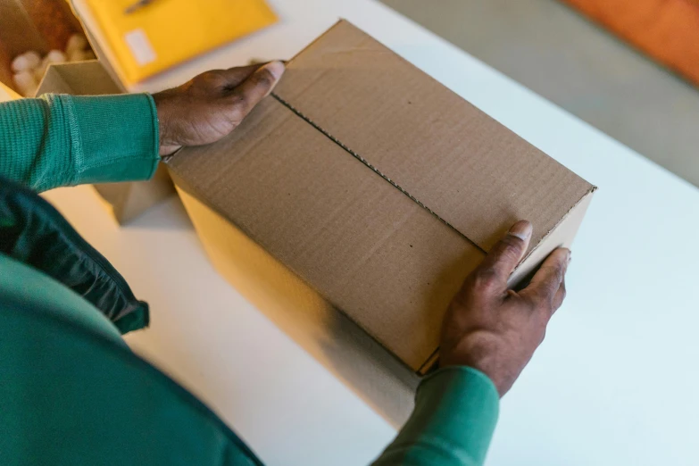 a person holding a box on a table, pexels contest winner, hurufiyya, gold and green, delivering mail, thick linings, thumbnail
