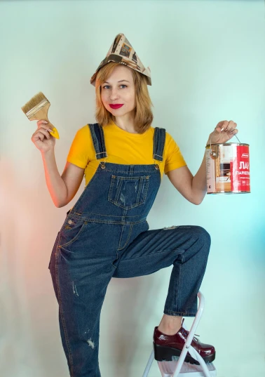 a woman in overalls holding a paintbrush and a paint can, by Julia Pishtar, pexels contest winner, parody work, gold clothes, 15081959 21121991 01012000 4k, jeans and t shirt