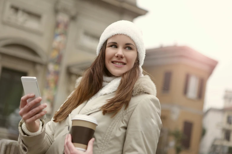 a woman holding a cup of coffee and a cell phone, a portrait, by Sebastian Vrancx, shutterstock, beanie, italian, walking down, 3945074687