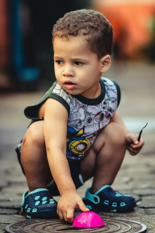 a little boy playing with a pink toy, a picture, by Joze Ciuha, pexels contest winner, graffiti, kneeling and looking up, dressed in a top and shorts, looking confused, gif