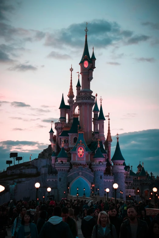 a crowd of people standing in front of a castle, inspired by disney, pexels contest winner, evening lighting, disney remake (2021), amusement park buildings, symmetrical image