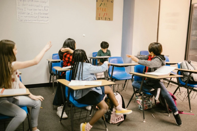 a group of children sitting at desks in a classroom, pexels contest winner, reaching out to each other, carson ellis, taejune kim, facing away from the camera