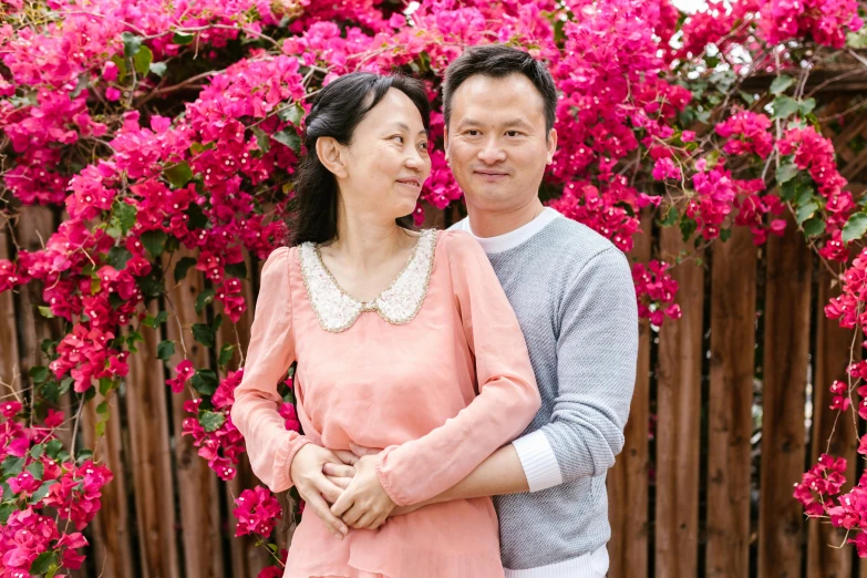 a man and woman standing next to each other in front of pink flowers, a portrait, inspired by Cui Bai, pexels contest winner, family friendly, casually dressed, wei wang, 38 years old