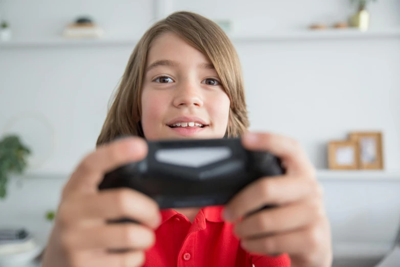 a young girl holding a video game controller, a picture, shutterstock, long hair and red shirt, young boy, aged 13, thumbnail