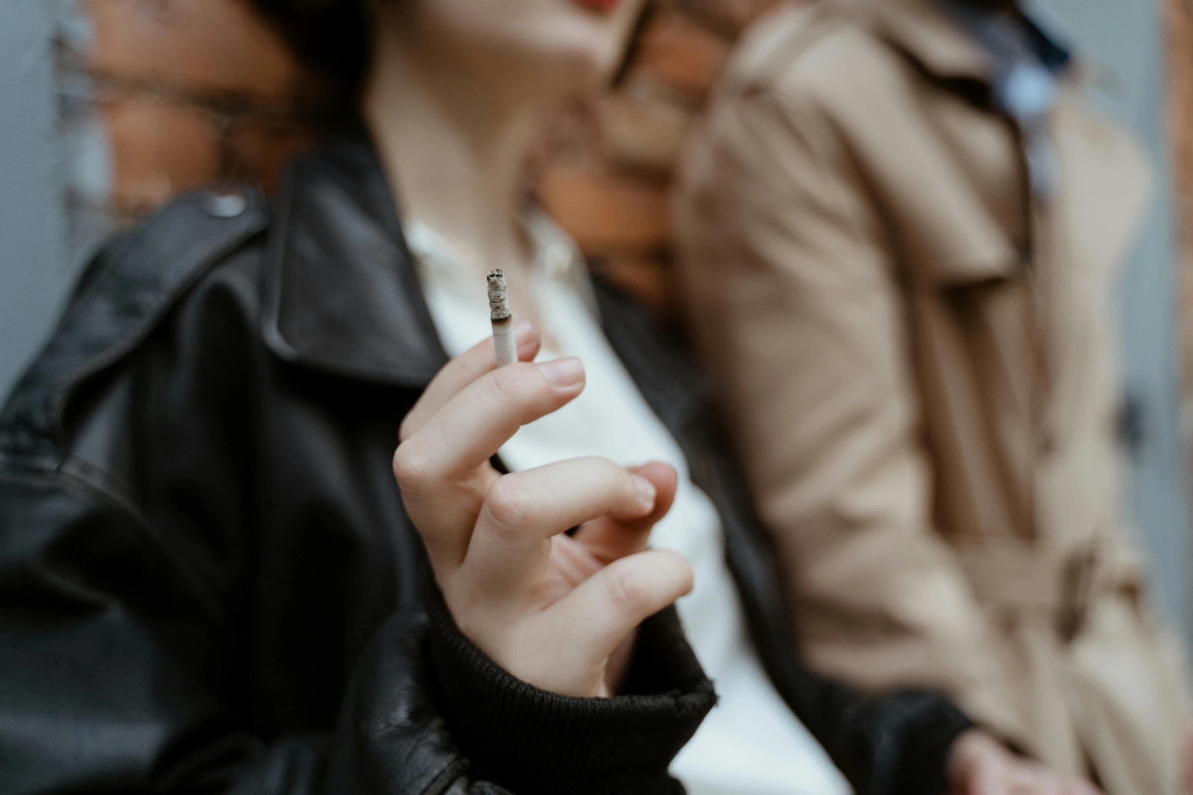 a close up of a person holding a cigarette, a picture, by Emma Andijewska, trending on pexels, wearing jacket, a group of people, sits on a finger, spikes on the body