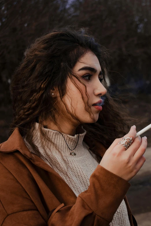 a woman smoking a cigarette in a park, inspired by Elsa Bleda, trending on pexels, renaissance, indian girl with brown skin, brown messy hair, wearing a turtleneck and jacket, profile pic