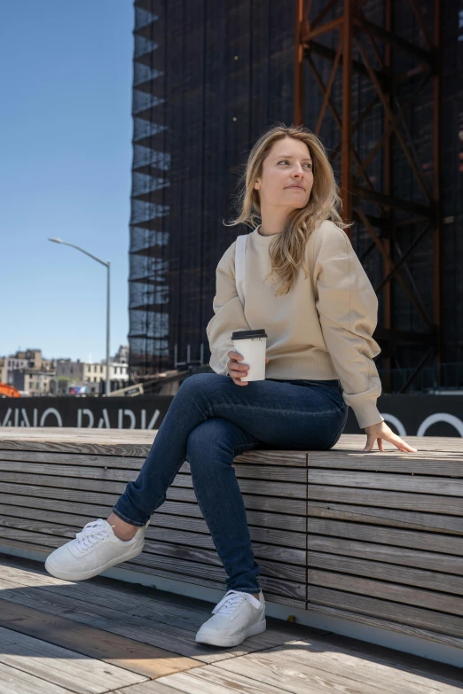 a woman sitting on a bench with a cup of coffee, casual streetwear, lynn skordal, light tan, engineered