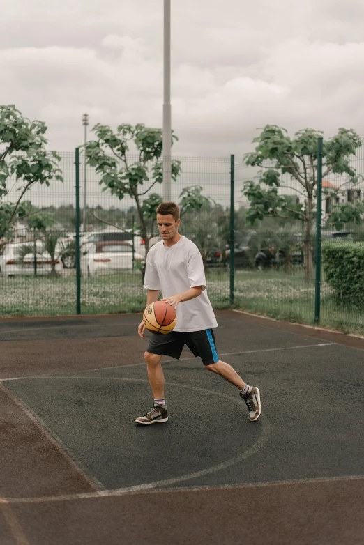 a man standing on a basketball court holding a basketball, by Attila Meszlenyi, trending on dribble, happening, wearing shorts and t shirt, running freely, in a suburb, sports setting