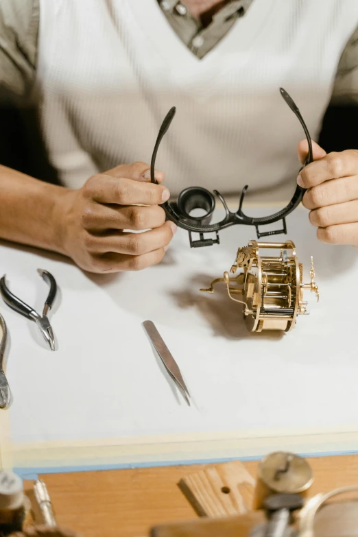 a person sitting at a table holding a pair of glasses, by Matthias Stom, trending on pexels, kinetic art, cogs and springs and jewels, assembly instructions, panorama, face covers half of the frame