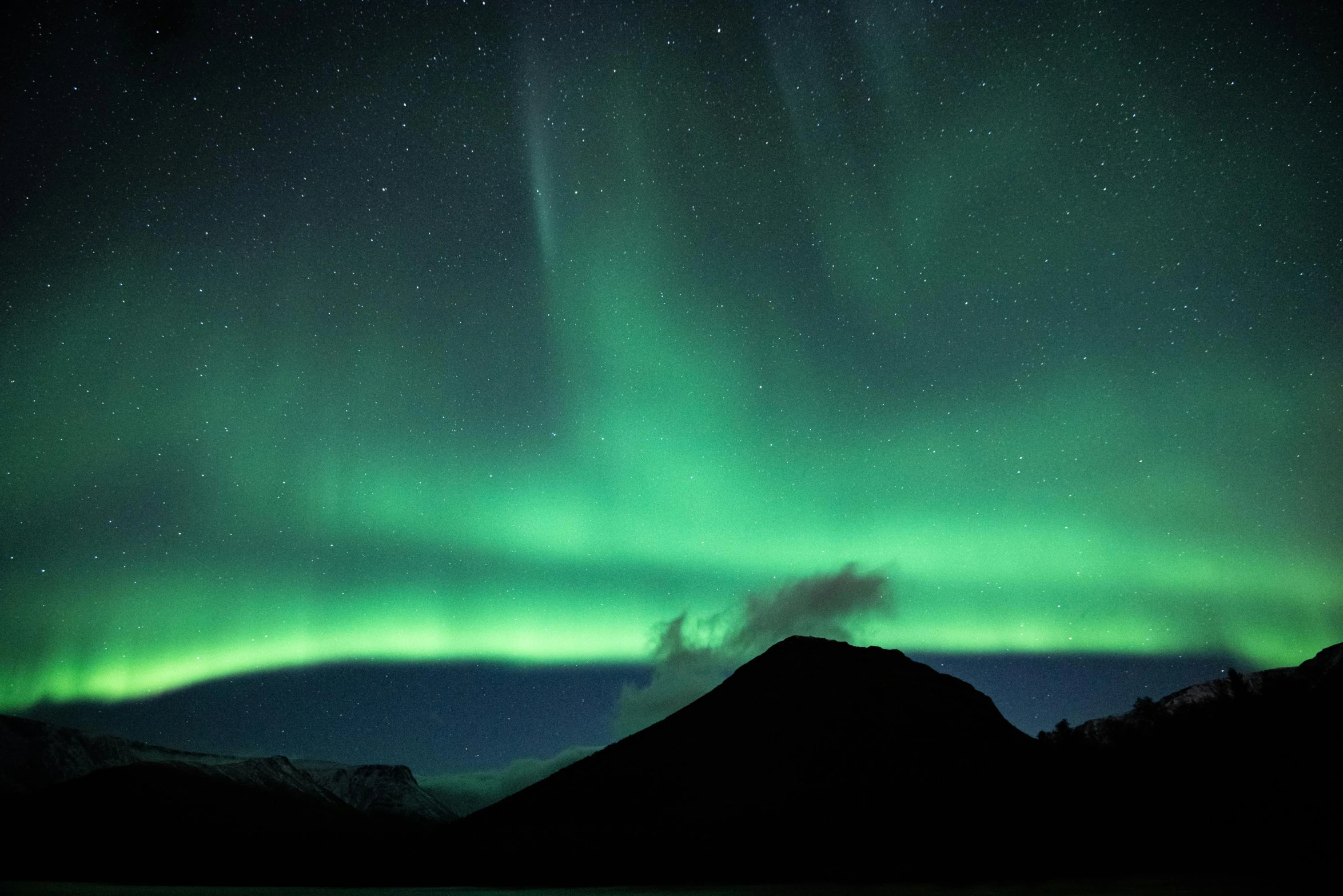 a large body of water with a mountain in the background, an album cover, trending on unsplash, hurufiyya, aurora borealis in the sky, green lights, black and green, james turrell