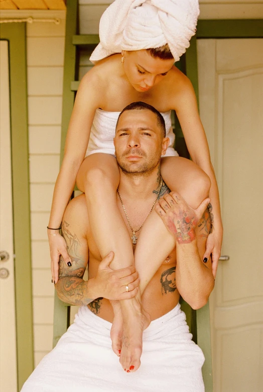 a woman sitting on top of a man in a towel, a tattoo, top - down photograph, lean man with light tan skin, woman holding another woman, hung above the door