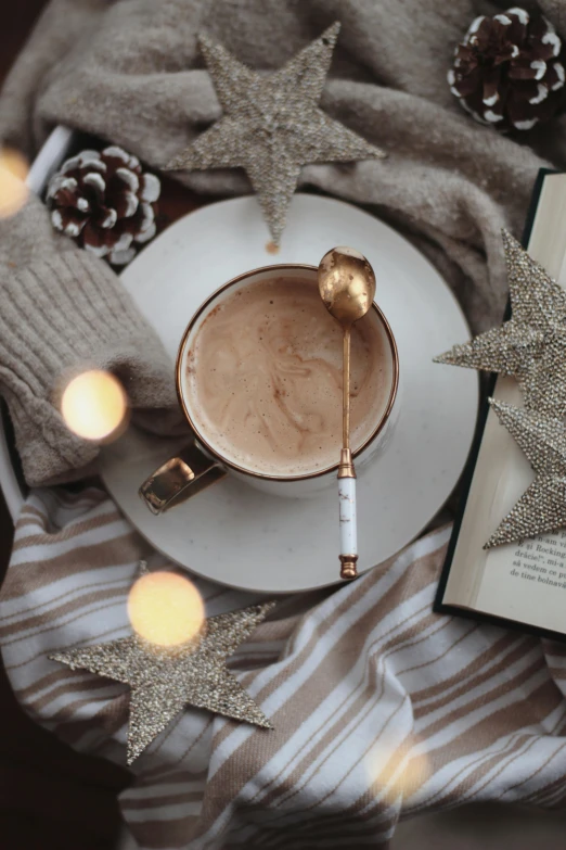 a book sitting on top of a table next to a cup of coffee, gold decorations, thumbnail, starry, hot cocoa drink