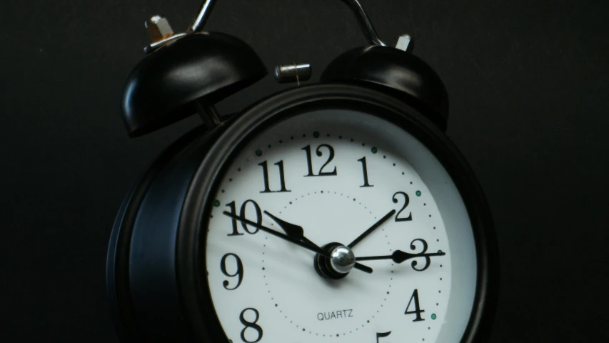 a black alarm clock sitting on top of a table, looking towards the camera, zoomed out shot, thumbnail, stacked image