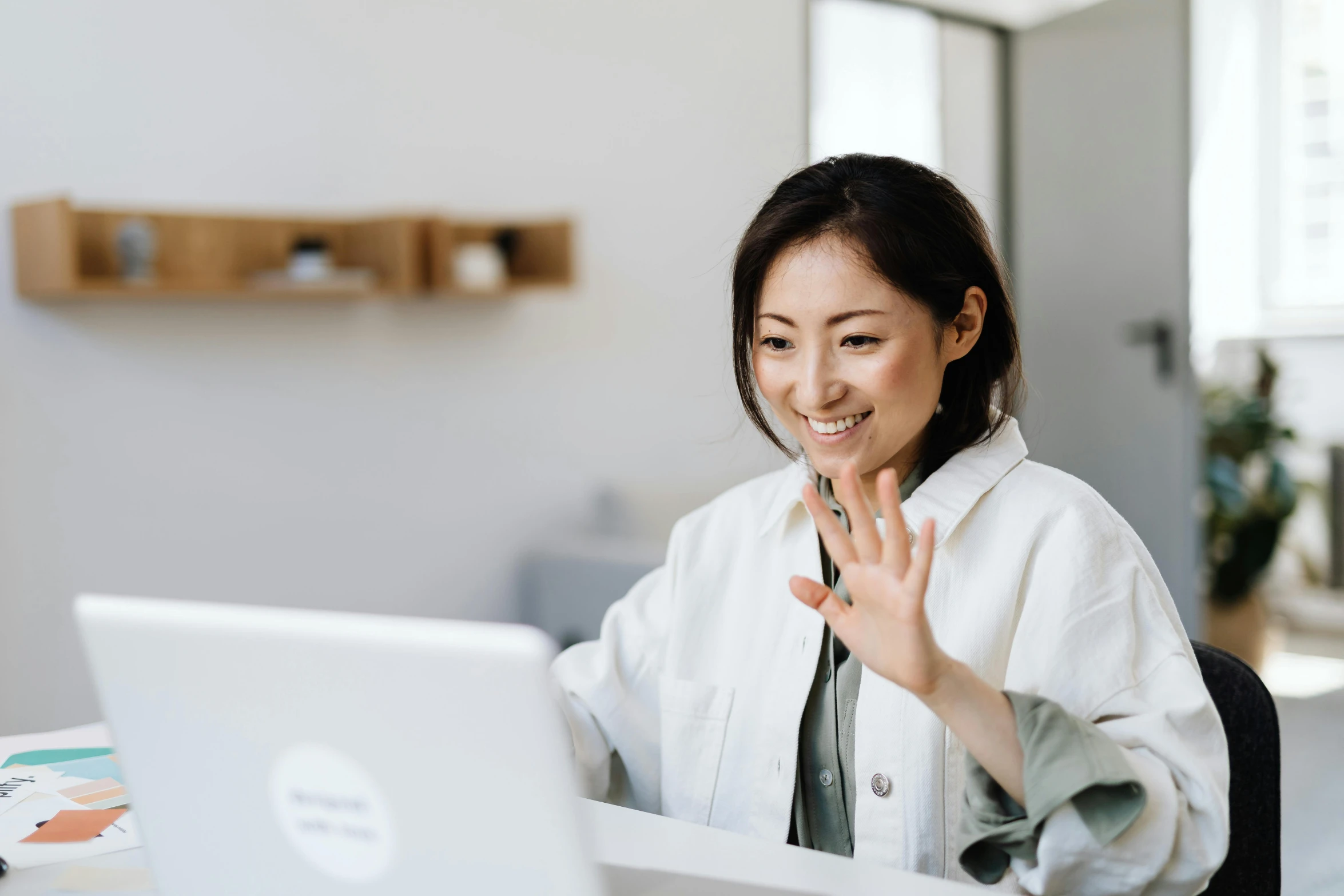 a woman sitting at a table in front of a laptop, inspired by helen huang, trending on pexels, hurufiyya, waving and smiling, ethnicity : japanese, nursing, calmly conversing 8k