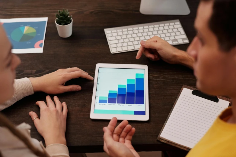 a couple of people sitting at a table with a tablet, trending on unsplash, analytical art, graphs, avatar image, bottom angle, official screenshot