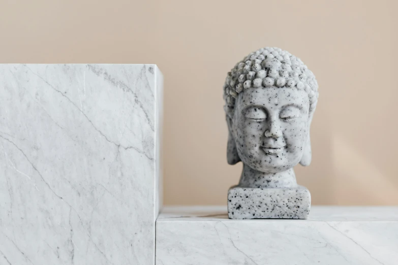 a statue sitting on top of a marble block, a marble sculpture, inspired by Kaigetsudō Ando, trending on pexels, square face, placed in a living room, detailed head, buddhist