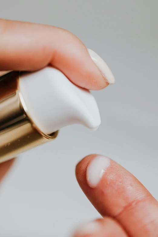 a close up of a person holding a bottle of liquid, white with gold accents, cosmetics, thumbnail, cream