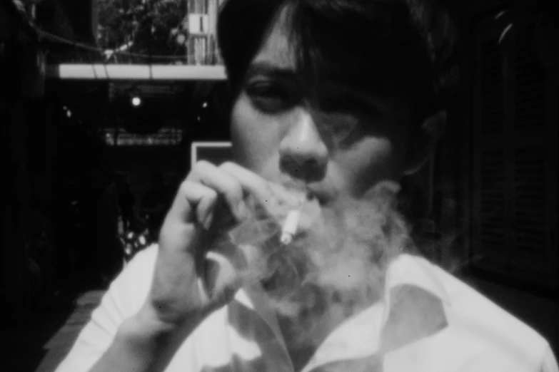 a black and white photo of a man smoking a cigarette, inspired by Shinji Aramaki, vhs footage still, 1970s philippines, still from a live action movie