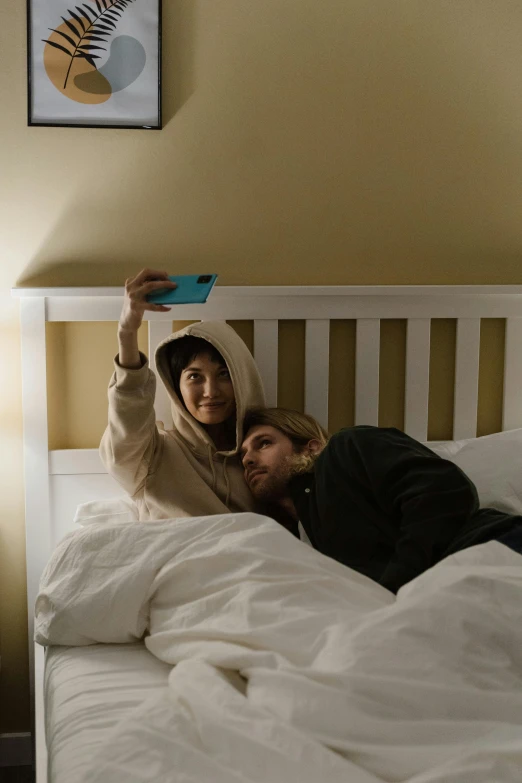 a couple of people laying on top of a bed, a polaroid photo, inspired by Elsa Bleda, trending on pexels, wearing an oversized hoodie, hold up smartphone, bo burnham, ignant