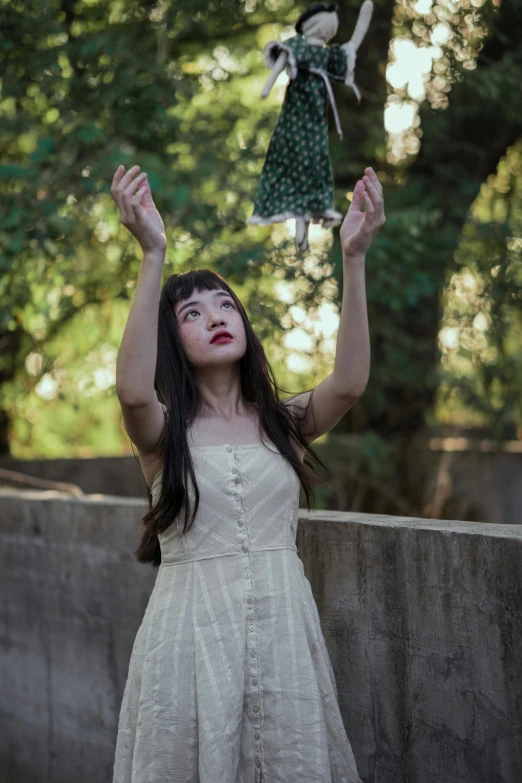 a woman in a white dress holding a doll above her head, an album cover, inspired by Kim Du-ryang, unsplash, melanie martinez, asian women, tattered green dress, outdoors