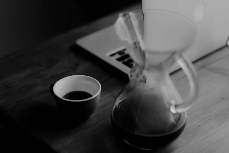 a coffee pot sitting on top of a wooden table next to a laptop, a black and white photo, by Karl Buesgen, unsplash, hourglass, chemistry, asleep, low light