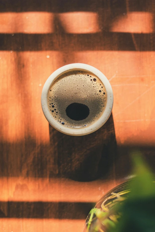 a cup of coffee sitting on top of a wooden table, by Niko Henrichon, trending on unsplash, huge black round hole, beer, eyes wide opened, full sun