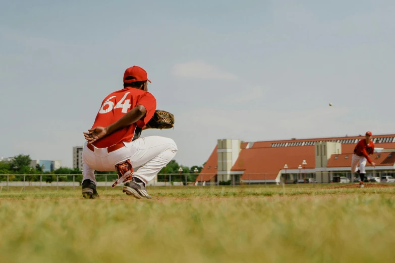 a baseball player kneeling on top of a field, a picture, by Andries Stock, pexels contest winner, red and white color theme, outside on the ground, panoramic, practice