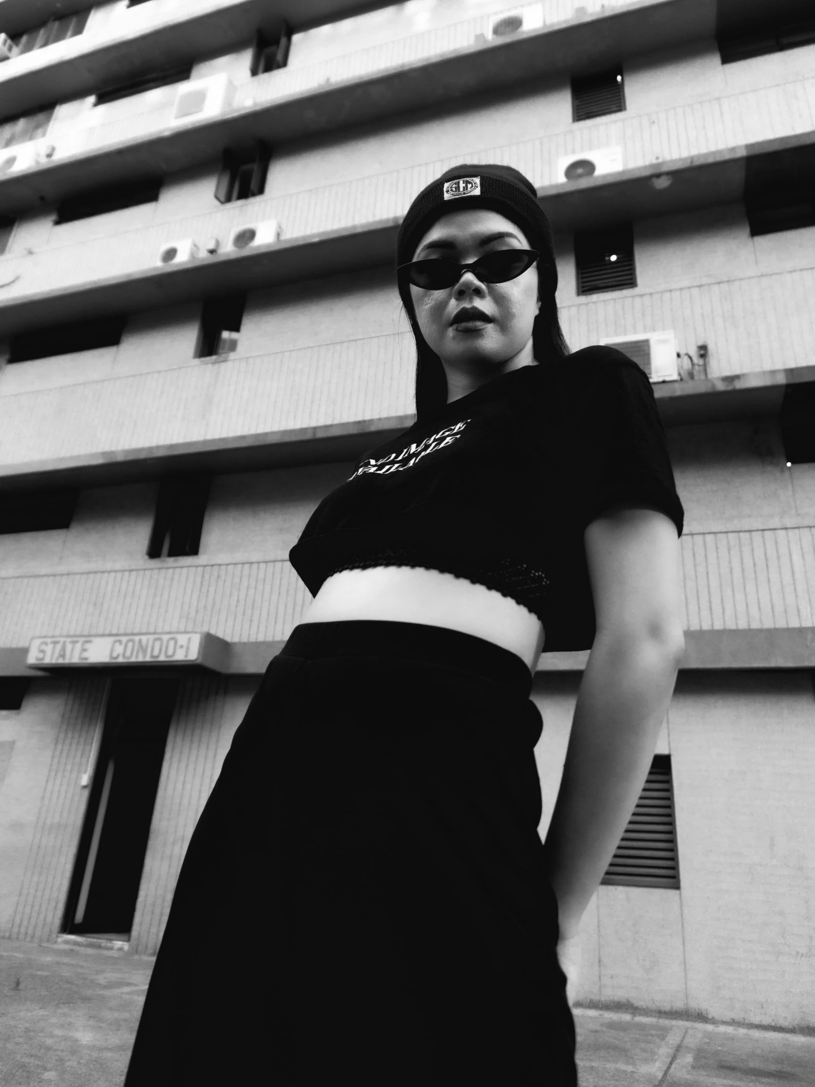 a woman standing in front of a tall building, a black and white photo, unsplash, lowbrow, wearing a black!! t - shirt, bladee from drain gang, hana yata, very aesthetic!!!!!!