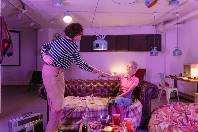 a man standing next to a woman sitting on a couch, by Helen Stevenson, purple scene lighting, batteries not included, charli bowater and artgeem, woman holding another woman