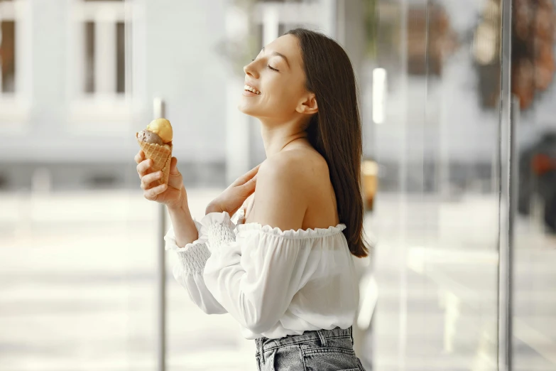a woman standing in front of a window eating an ice cream cone, trending on pexels, decolletage, oiled skin, at a mall, background image