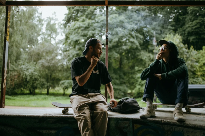 a couple of men sitting next to each other on a bench, by Emma Andijewska, pexels contest winner, skateboarder style, looking outside, smoking a blunt, sitting in the forrest