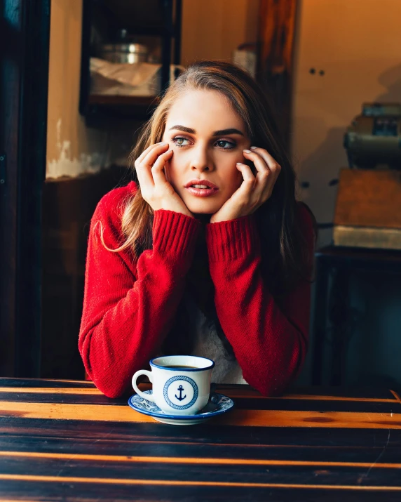 a woman sitting at a table with a cup of coffee, a portrait, inspired by Elsa Bleda, trending on unsplash, fine art, portrait of annasophia robb, frown fashion model, in a pub, red