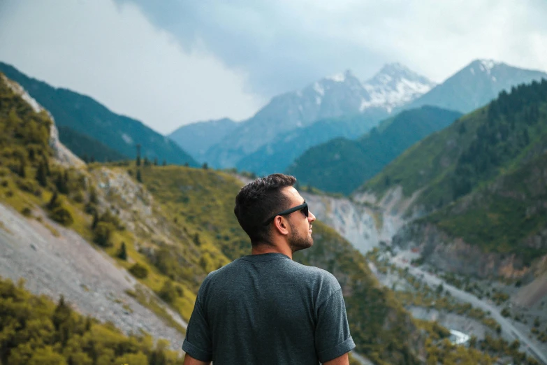 a man standing on top of a mountain looking at a valley, pexels contest winner, profile image, wearing oakley sunglasses, handsome man, ash thorp khyzyl saleem