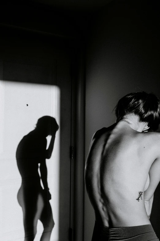 a black and white photo of a man standing in front of a mirror, a black and white photo, by Michael Sittow, muscular and exhausted woman, morning light showing injuries, the sun at their back, queer woman