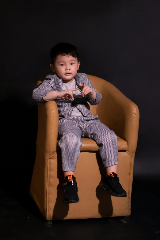 a little boy that is sitting in a chair, inspired by Xia Yong, pexels contest winner, neo-dada, grey pants and black dress shoes, wearing a track suit, leather clothing, reuben wu