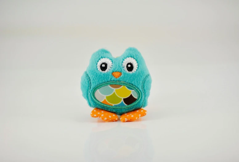 a stuffed owl sitting on top of a white surface, turquoise and orange, 35 mm product photo”, toddler, multi - coloured