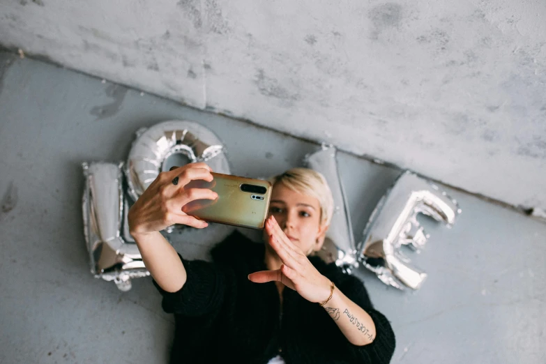 a woman taking a picture of herself with her phone, a photo, by Julia Pishtar, trending on pexels, love is the most relevant theme, wearing silver hair, woman holding sign, flatlay