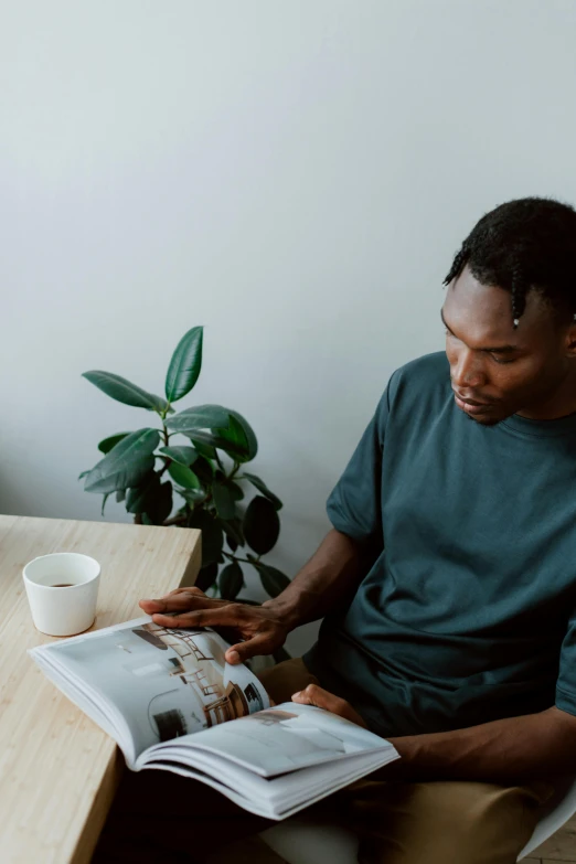 a man sitting at a table reading a magazine, pexels contest winner, man is with black skin, next to a plant, portrait of morning coffee, gif