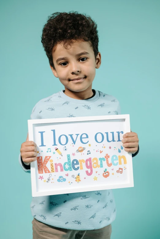 a young boy holding a sign that says i love our kindergarten, inspired by Kun Can, shutterstock contest winner, white frame, full colour print, hero shot, - i