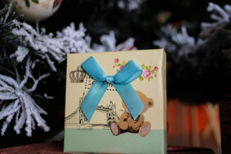 a present sitting on top of a table next to a christmas tree, product image, yellow and blue ribbons, london, cute pout