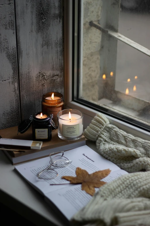 a book sitting on top of a window sill next to a candle, a picture, trending on pexels, late autumn, studio shot, serene smile, waxy candles